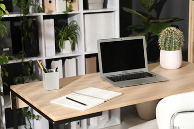 Photo of Stylish workplace with laptop, stationery and floral decor in office. Biophilic interior design