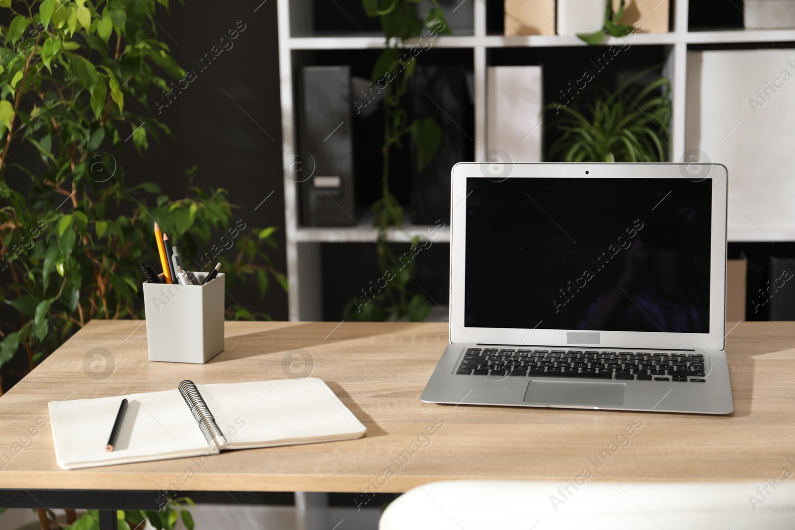 Stylish workplace with laptop, stationery and floral decor in office. Biophilic interior design Photo of Stylish workplace with laptop, stationery and floral decor in office. Biophilic interior design