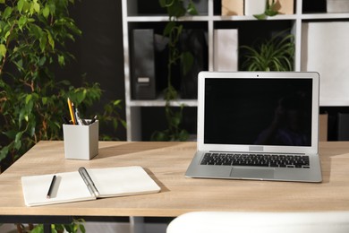 Photo of Stylish workplace with laptop, stationery and floral decor in office. Biophilic interior design
