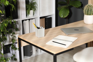 Photo of Stylish workplace with laptop, stationery and floral decor in office. Biophilic interior design