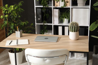 Photo of Stylish workplace with laptop, stationery and floral decor in office. Biophilic interior design