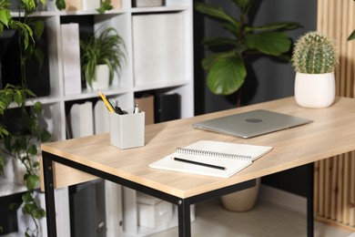 Photo of Stylish workplace with laptop, stationery and floral decor in office. Biophilic interior design