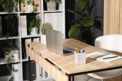 Photo of Stylish workplace with laptop, stationery and floral decor in office. Biophilic interior design