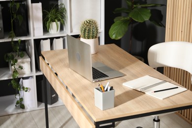 Photo of Stylish workplace with laptop, stationery and floral decor in office. Biophilic interior design