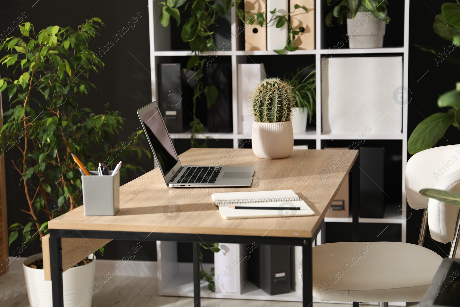Stylish workplace with laptop, stationery and floral decor in office. Biophilic interior design Photo of Stylish workplace with laptop, stationery and floral decor in office. Biophilic interior design