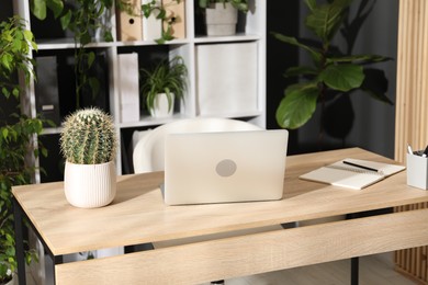 Photo of Stylish workplace with laptop, stationery and floral decor in office. Biophilic interior design
