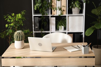 Photo of Stylish workplace with laptop, stationery and floral decor in office. Biophilic interior design