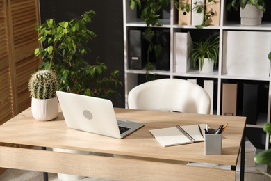 Photo of Stylish workplace with laptop, stationery and floral decor in office. Biophilic interior design