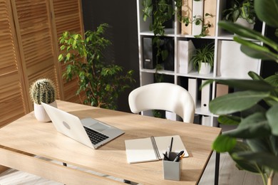 Photo of Stylish workplace with laptop, stationery and floral decor in office. Biophilic interior design