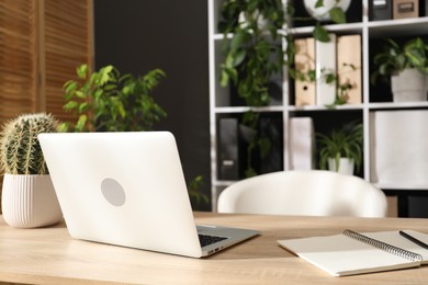 Photo of Stylish workplace with laptop, stationery and floral decor in office, closeup. Biophilic interior design