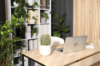 Photo of Stylish workplace with laptop, stationery and floral decor in office. Biophilic interior design