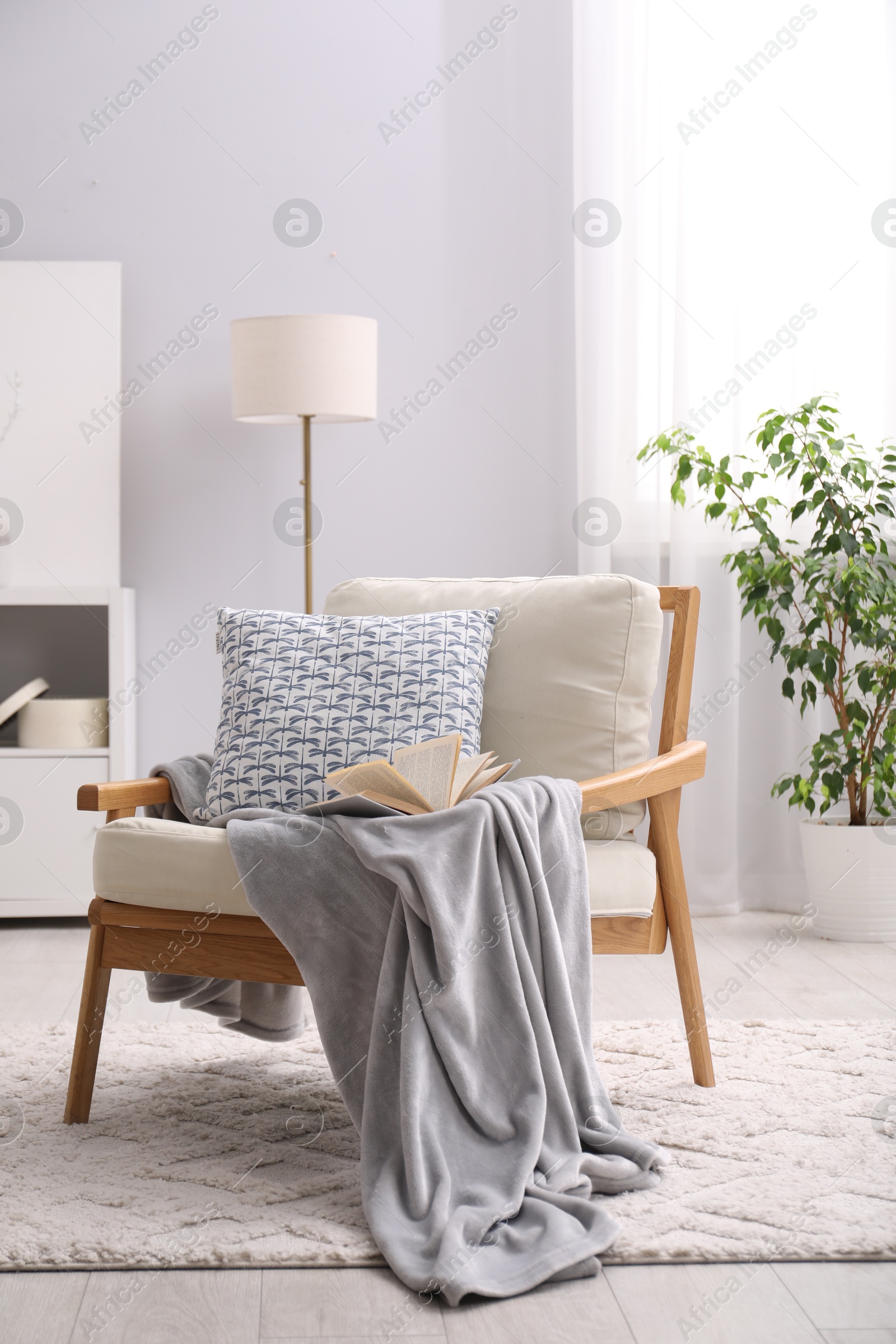 Photo of Comfortable armchair with book, pillow and blanket in living room. Interior design
