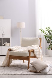 Photo of Comfortable armchair with blanket in living room. Interior design