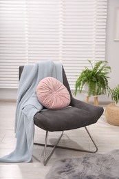 Photo of Comfortable grey armchair with pink pillow and blanket in living room. Interior design