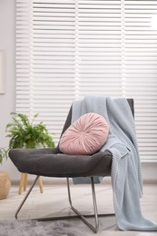 Photo of Comfortable grey armchair with pink pillow and blanket in living room. Interior design
