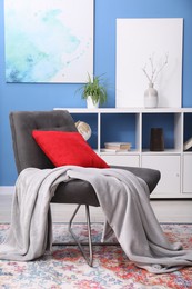 Photo of Comfortable grey armchair with red pillow and blanket in living room. Interior design