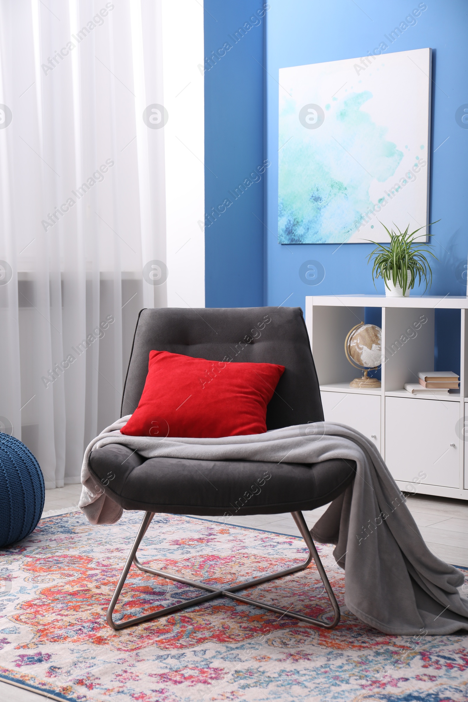 Photo of Comfortable grey armchair with red pillow and blanket in living room. Interior design
