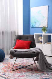 Photo of Comfortable grey armchair with red pillow and blanket in living room. Interior design