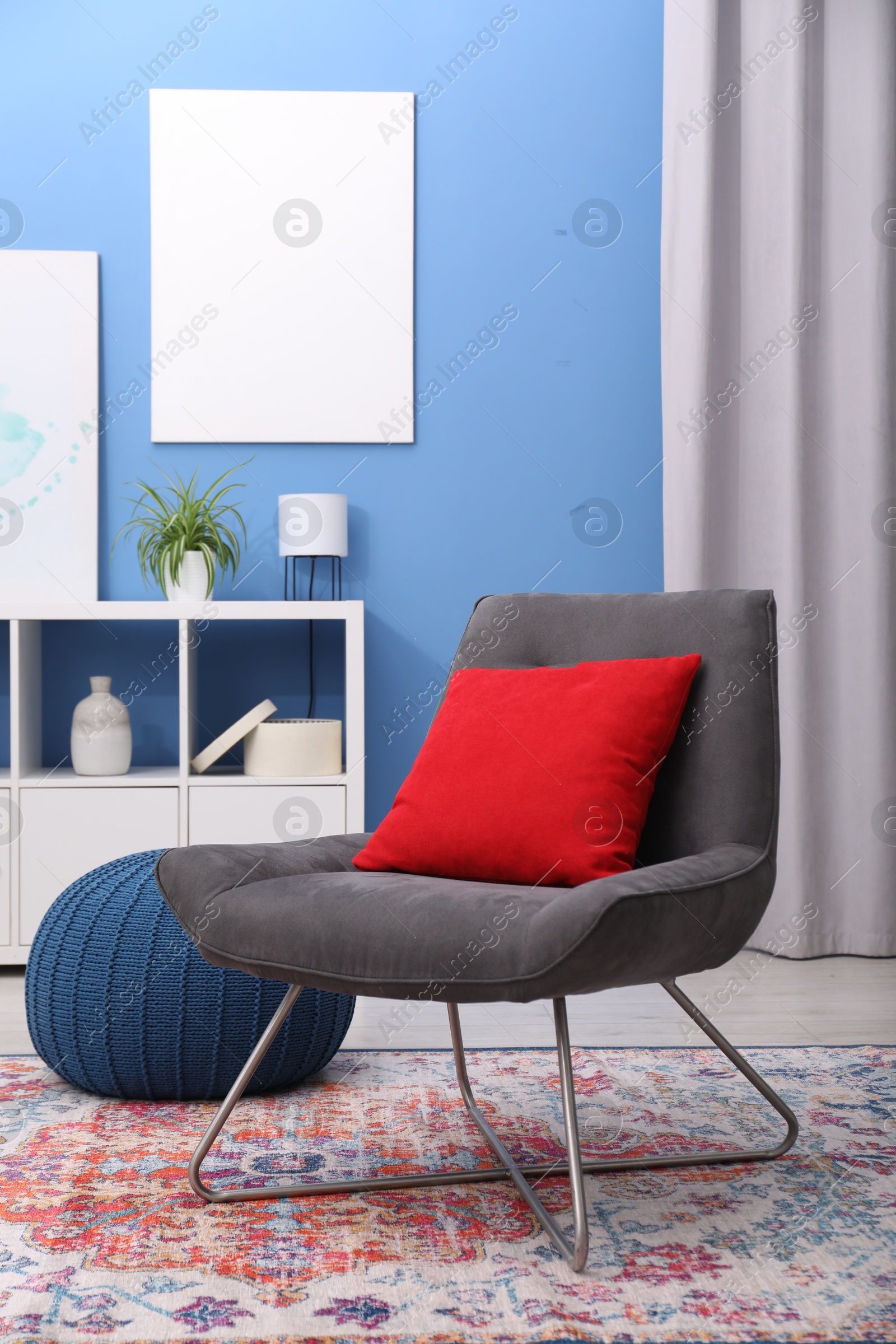 Photo of Comfortable grey armchair with red pillow in living room. Interior design