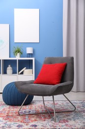 Photo of Comfortable grey armchair with red pillow in living room. Interior design