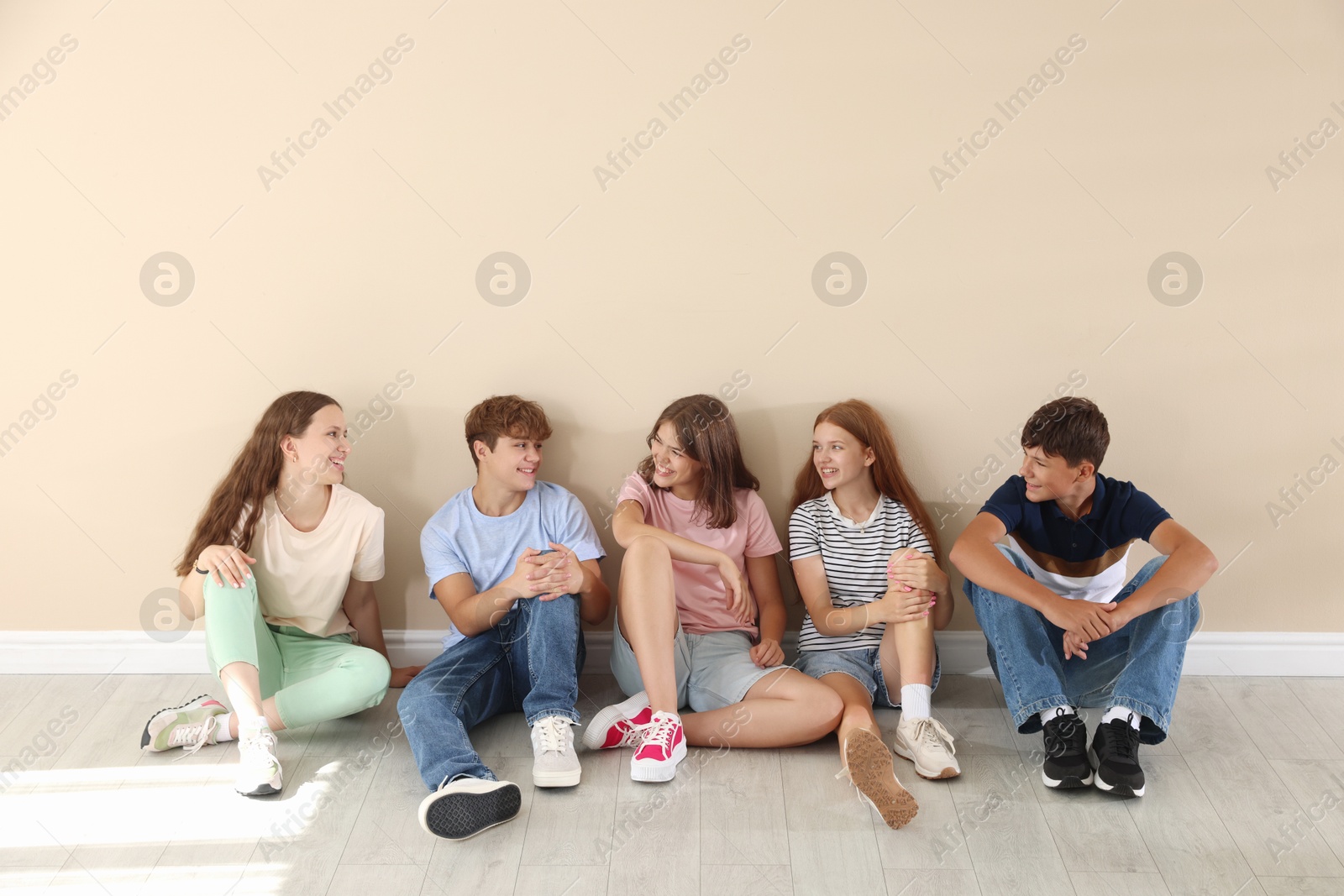 Photo of Happy teenage friends sitting on floor near beige wall indoors