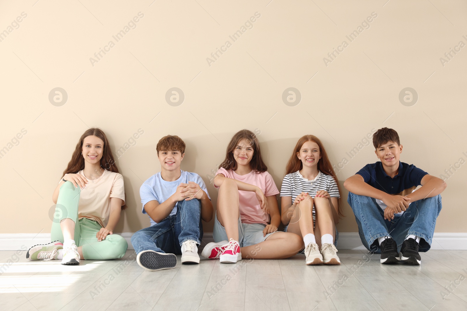 Photo of Happy teenage friends sitting on floor near beige wall indoors