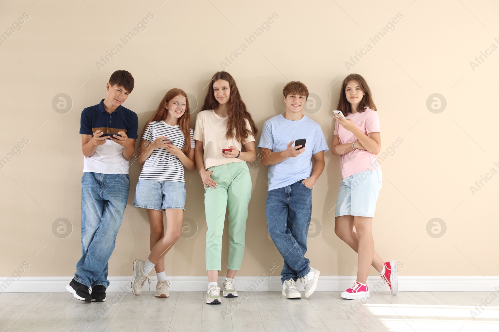 Photo of Teenage friends with smartphones near beige wall indoors