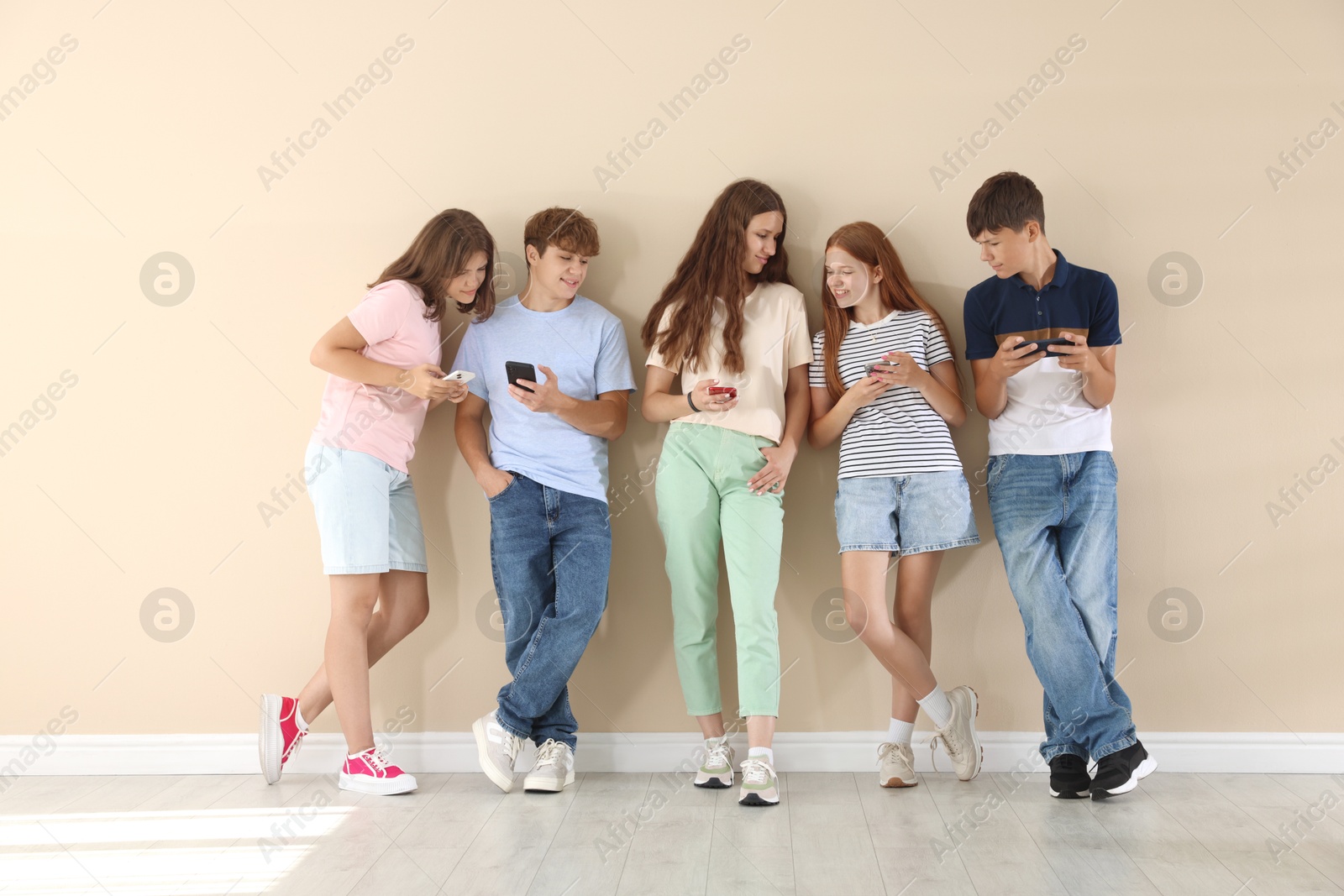 Photo of Teenage friends with smartphones near beige wall indoors