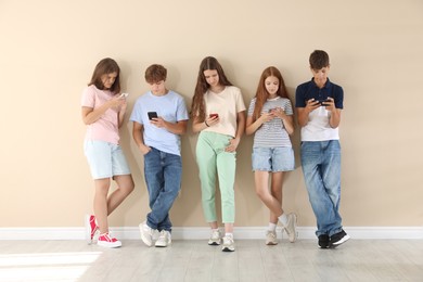 Photo of Teenage friends with smartphones near beige wall indoors
