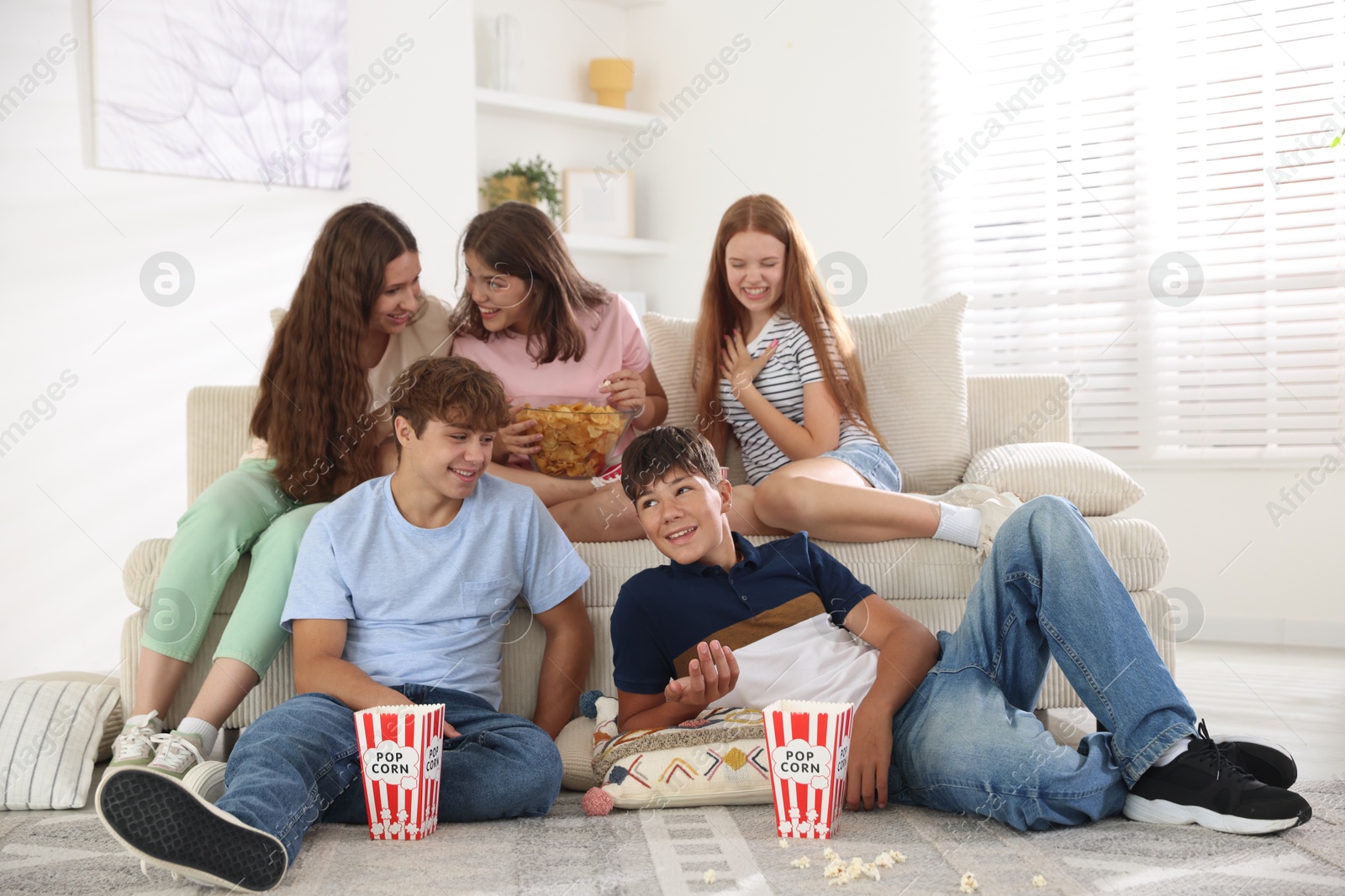 Photo of Happy teenage friends with snacks watching movie indoors