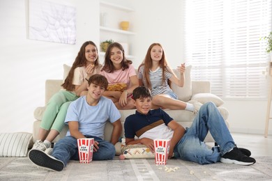 Photo of Happy teenage friends with snacks watching movie indoors