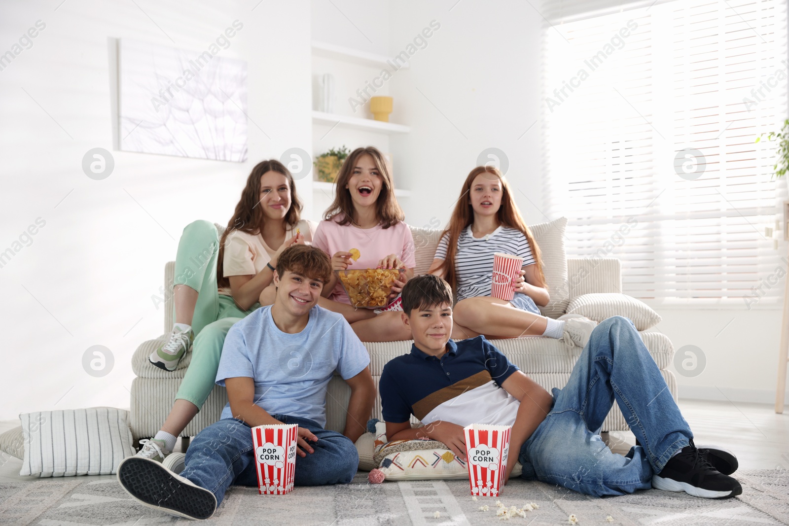Photo of Happy teenage friends with snacks watching movie indoors