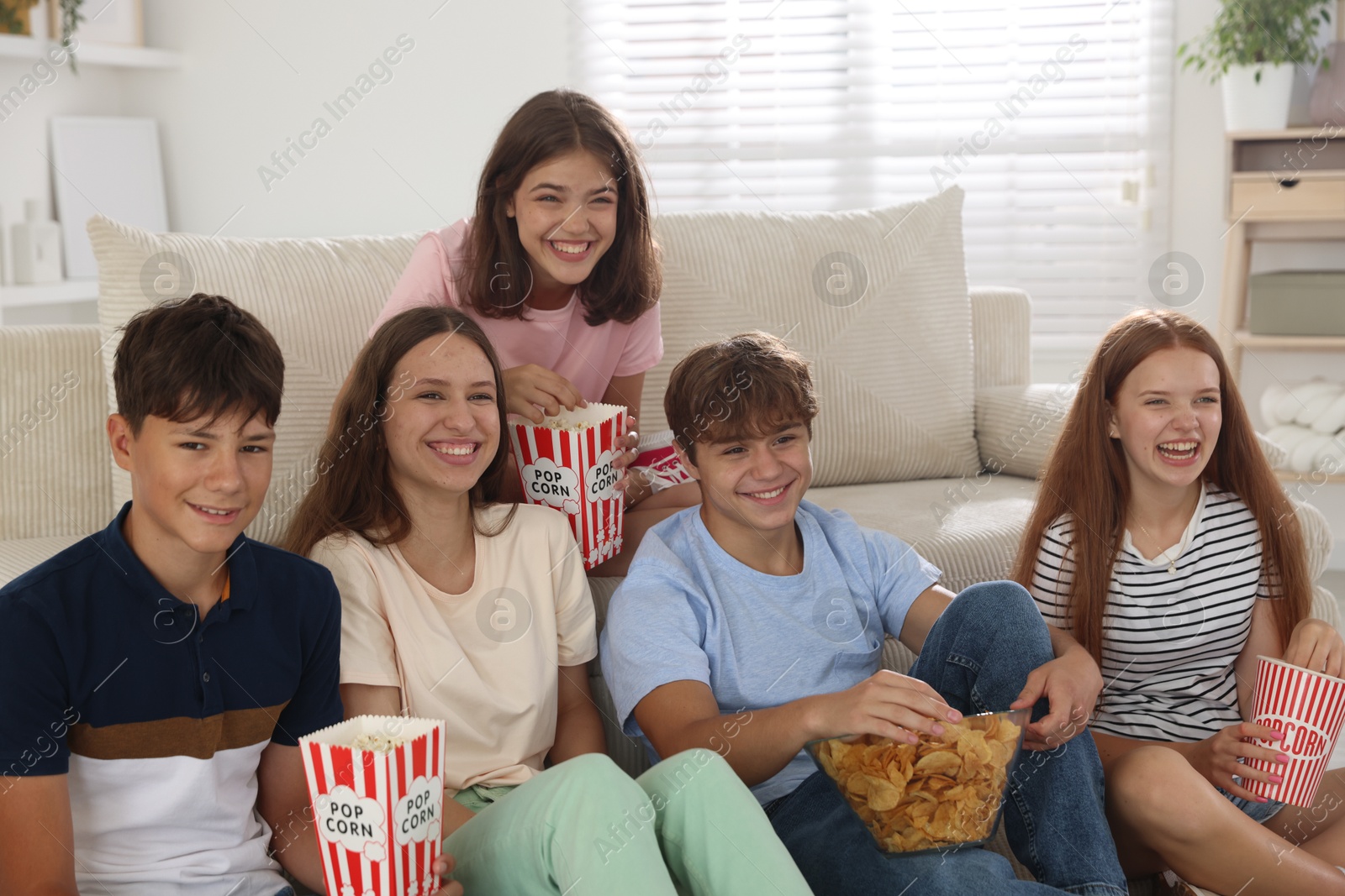 Photo of Happy teenage friends with snacks watching movie indoors