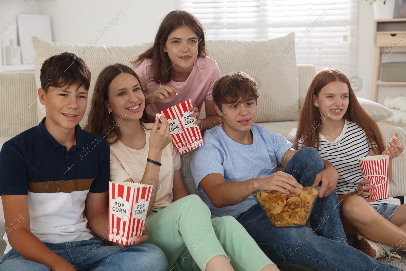 Photo of Happy teenage friends with snacks watching movie indoors