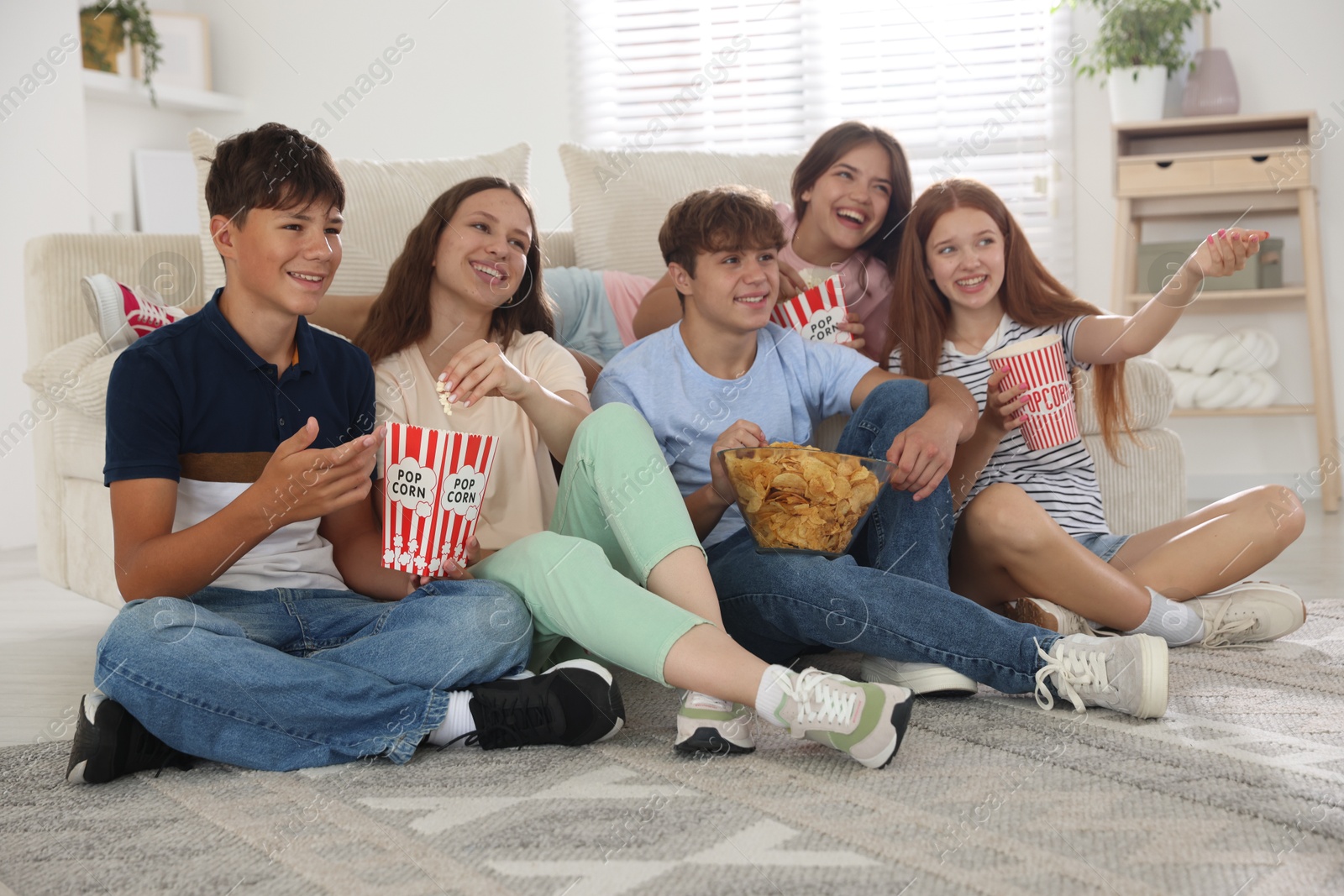 Photo of Happy teenage friends with snacks watching movie indoors