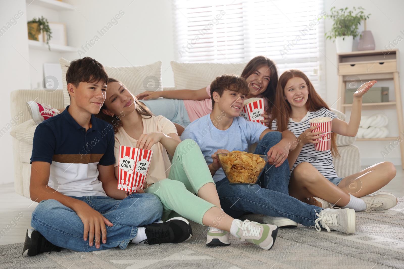 Photo of Happy teenage friends with snacks watching movie indoors