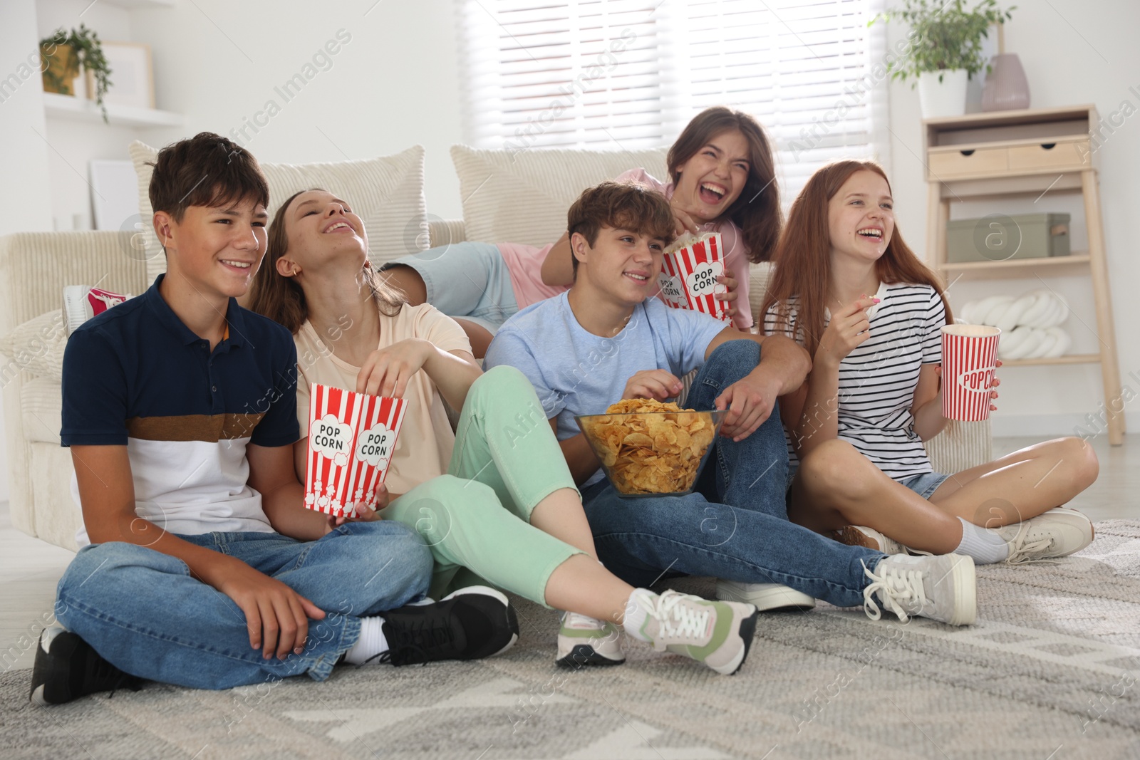 Photo of Happy teenage friends with snacks watching movie indoors