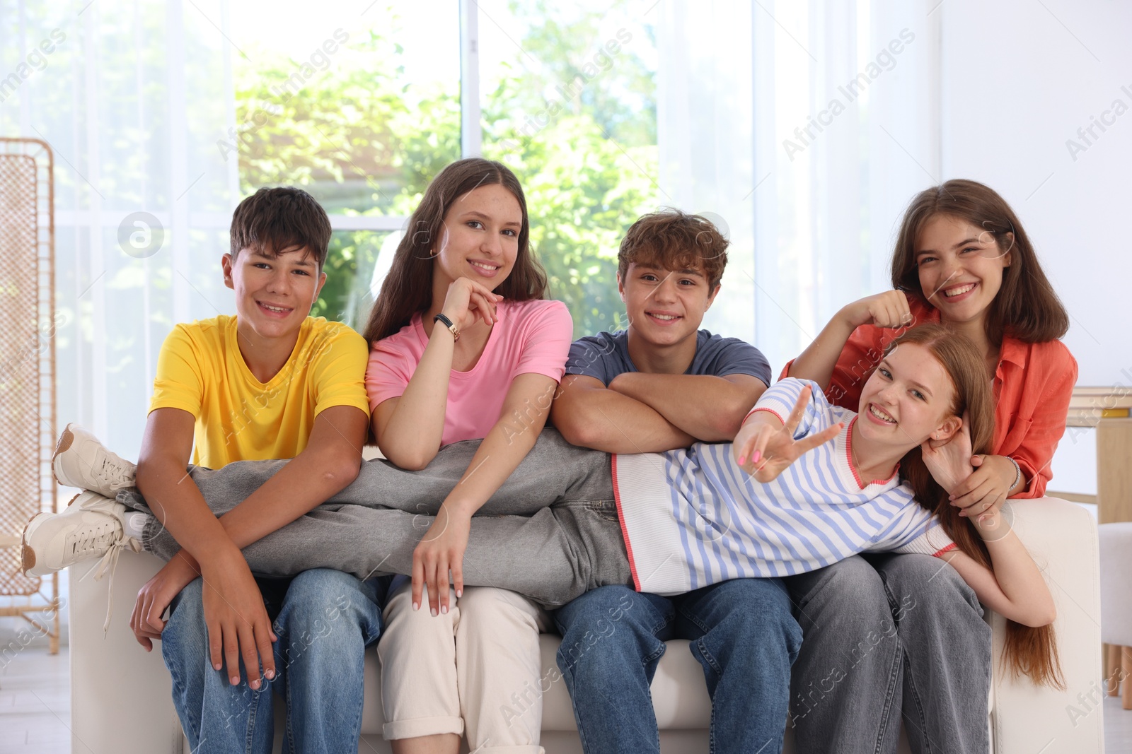 Photo of Happy teenage friends sitting on sofa indoors