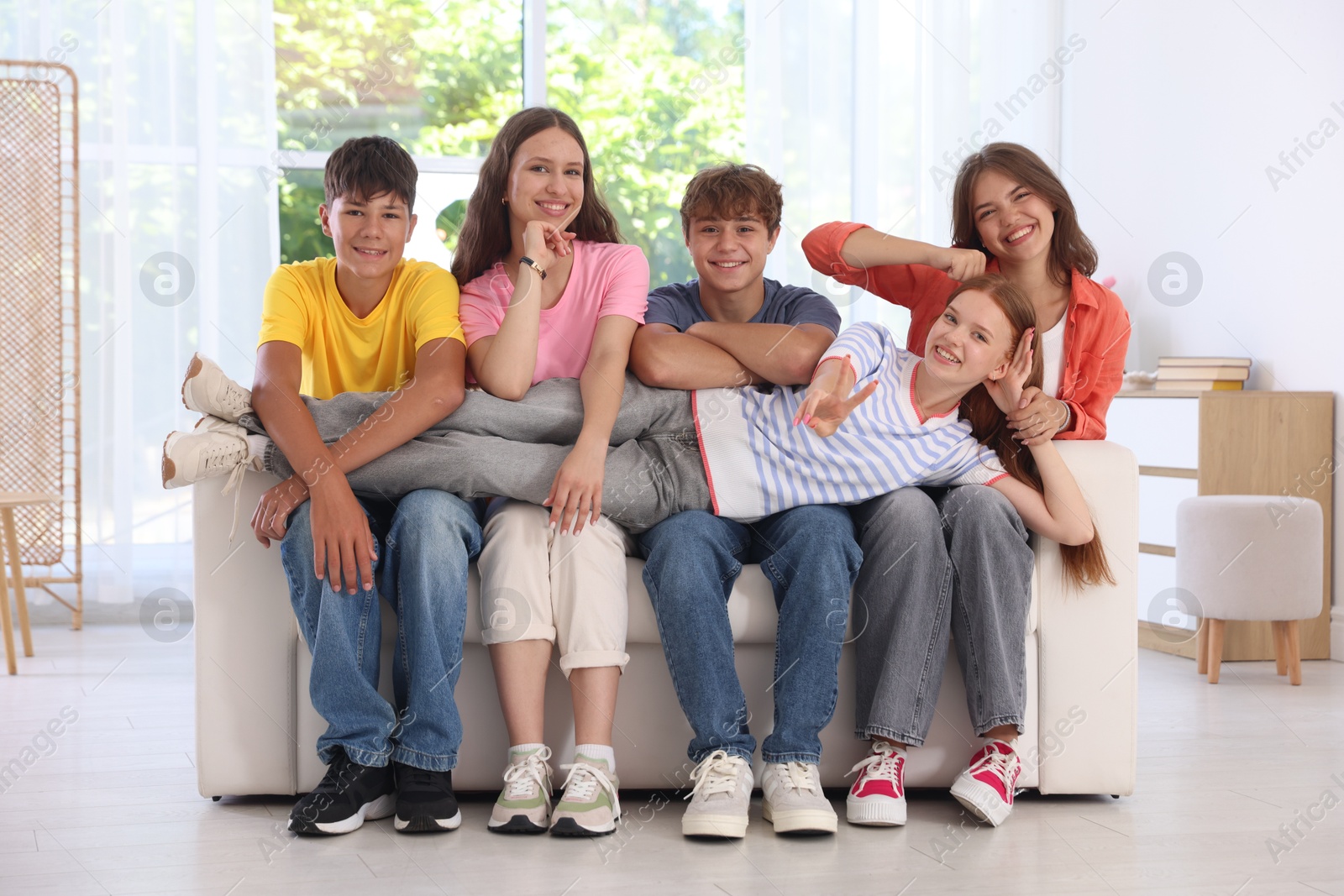 Photo of Happy teenage friends sitting on sofa indoors