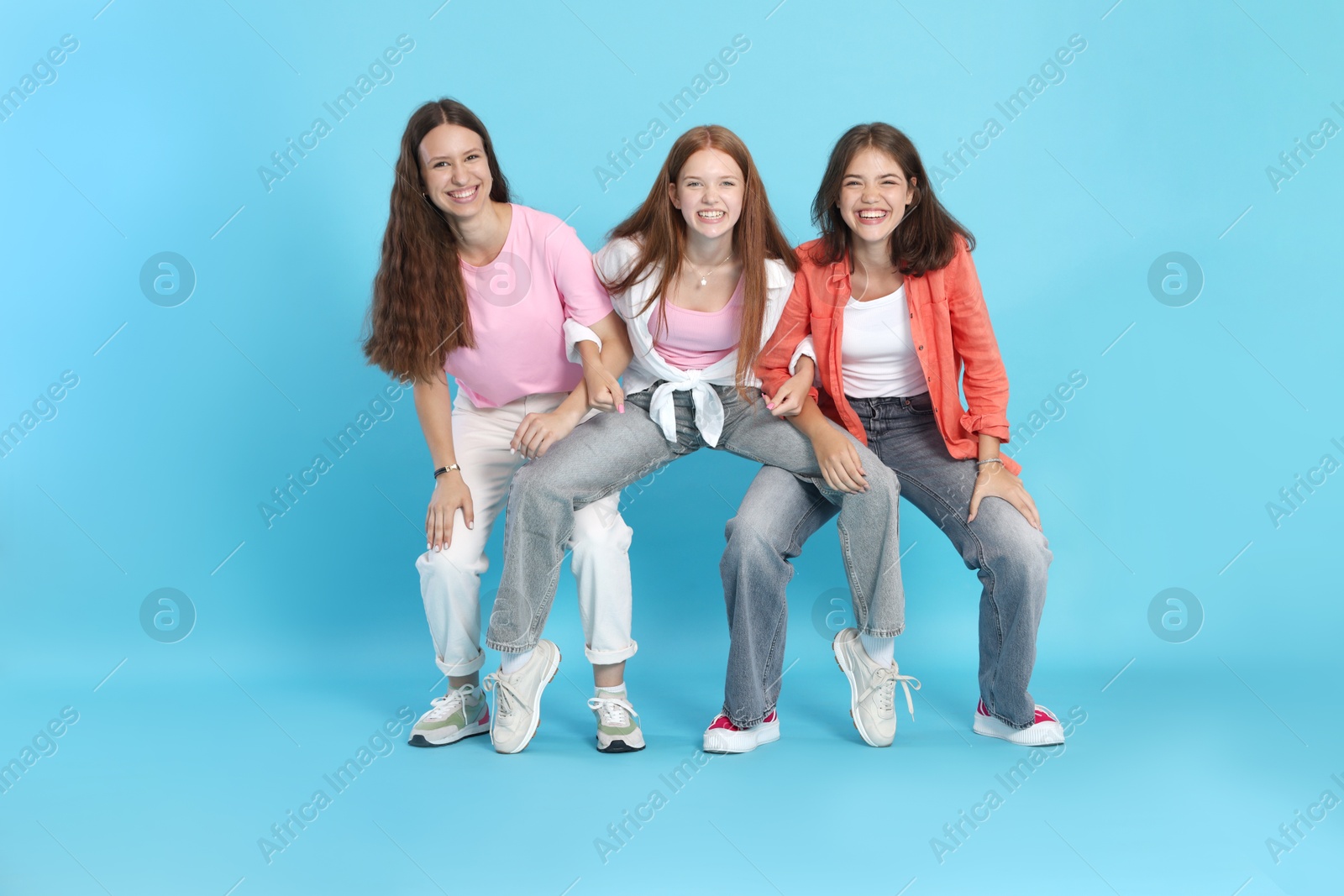 Photo of Full-length portrait of happy teenage friends on light blue background