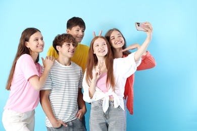 Photo of Happy teenage friends taking selfie with smartphone on light blue background