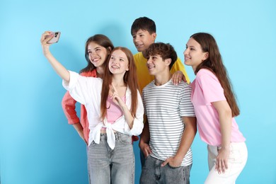 Photo of Happy teenage friends taking selfie with smartphone on light blue background