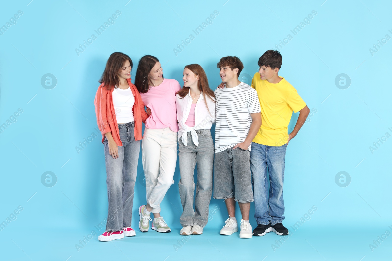 Photo of Full-length portrait of happy teenage friends on light blue background