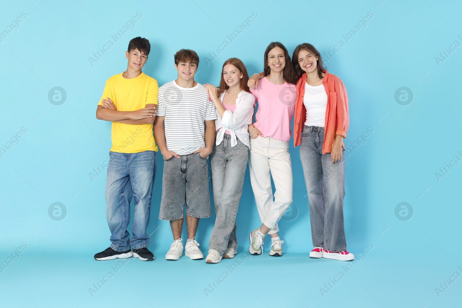 Photo of Full-length portrait of happy teenage friends on light blue background