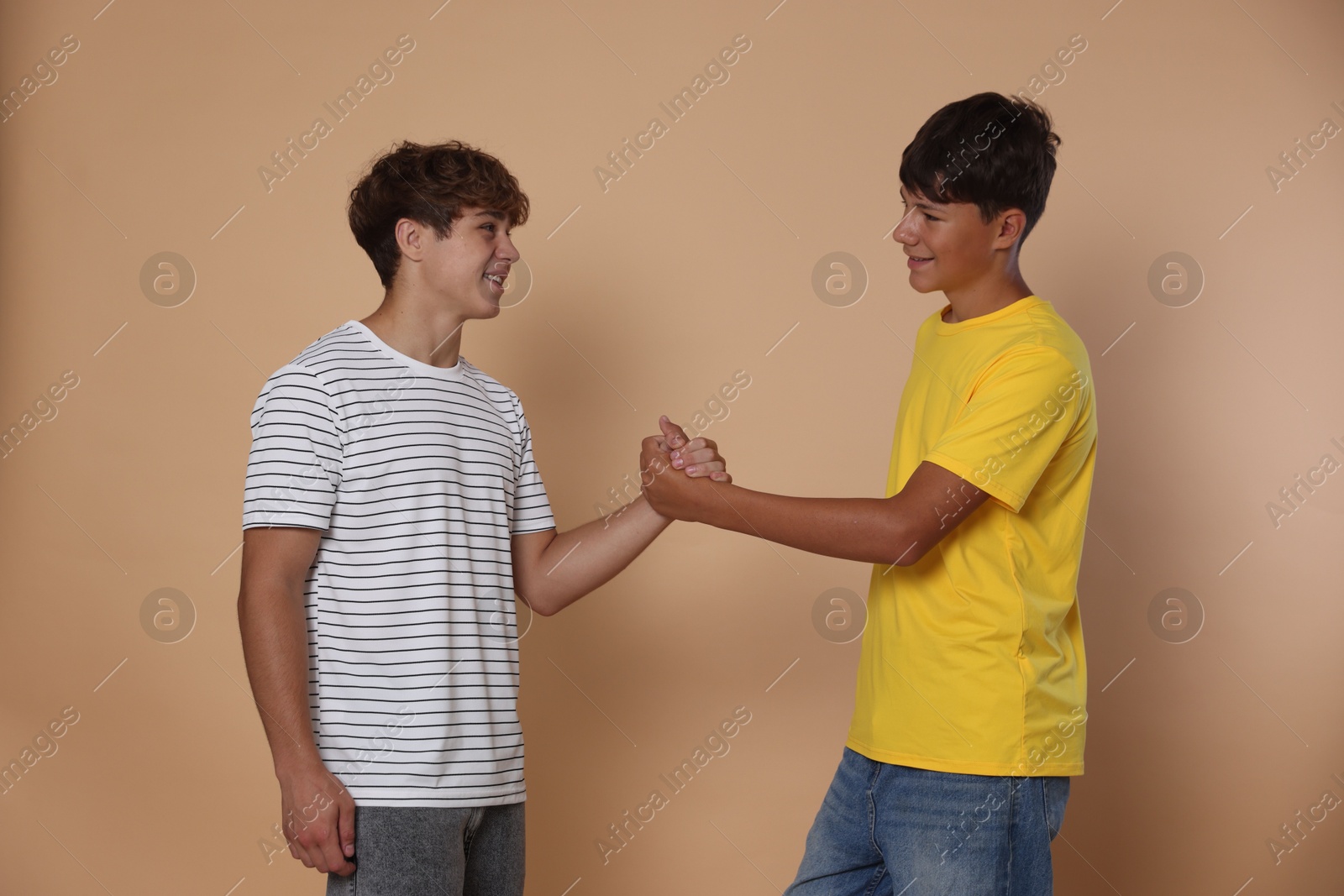 Photo of Friends. Two teenage boys shaking hands on beige background