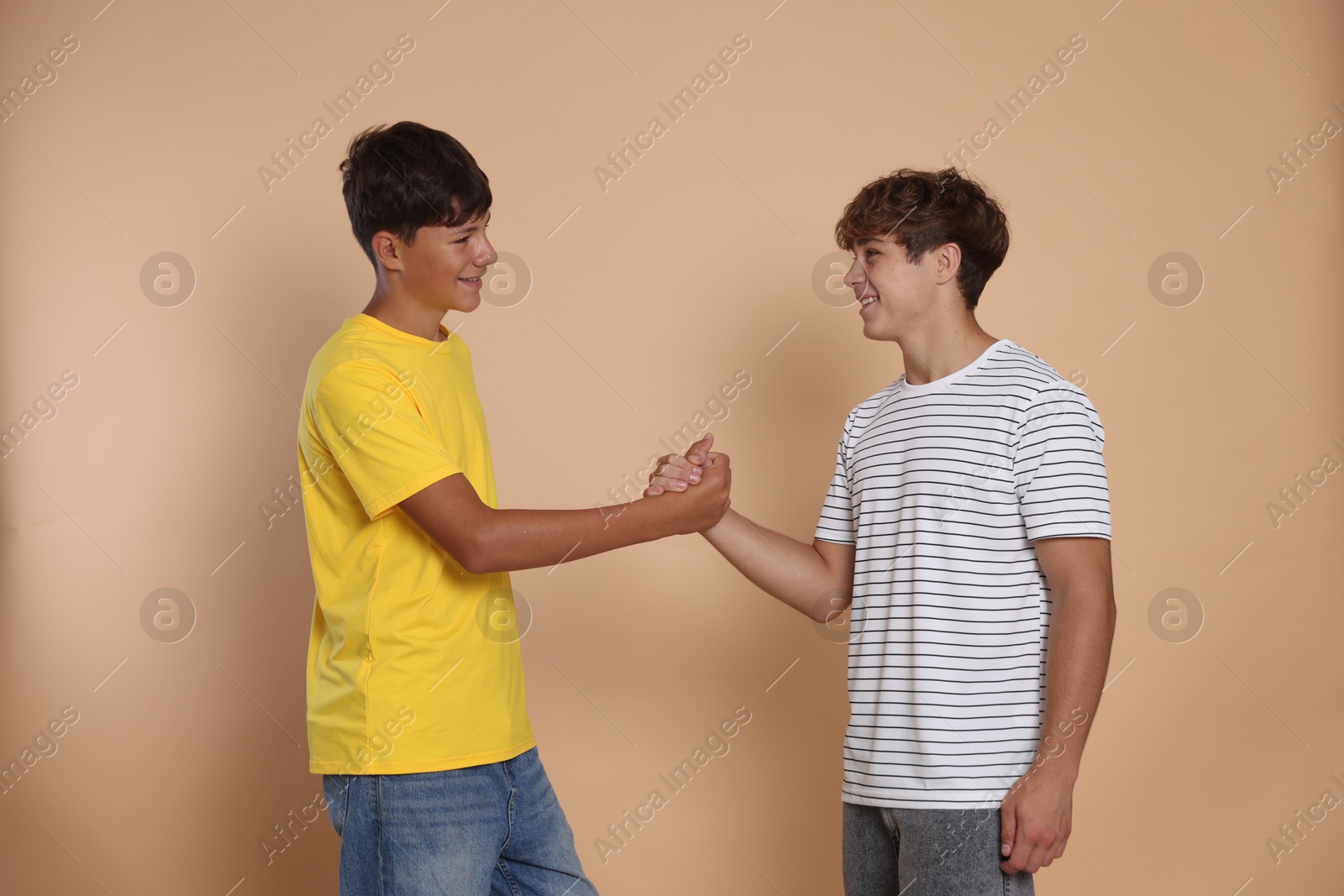 Photo of Friends. Two teenage boys shaking hands on beige background