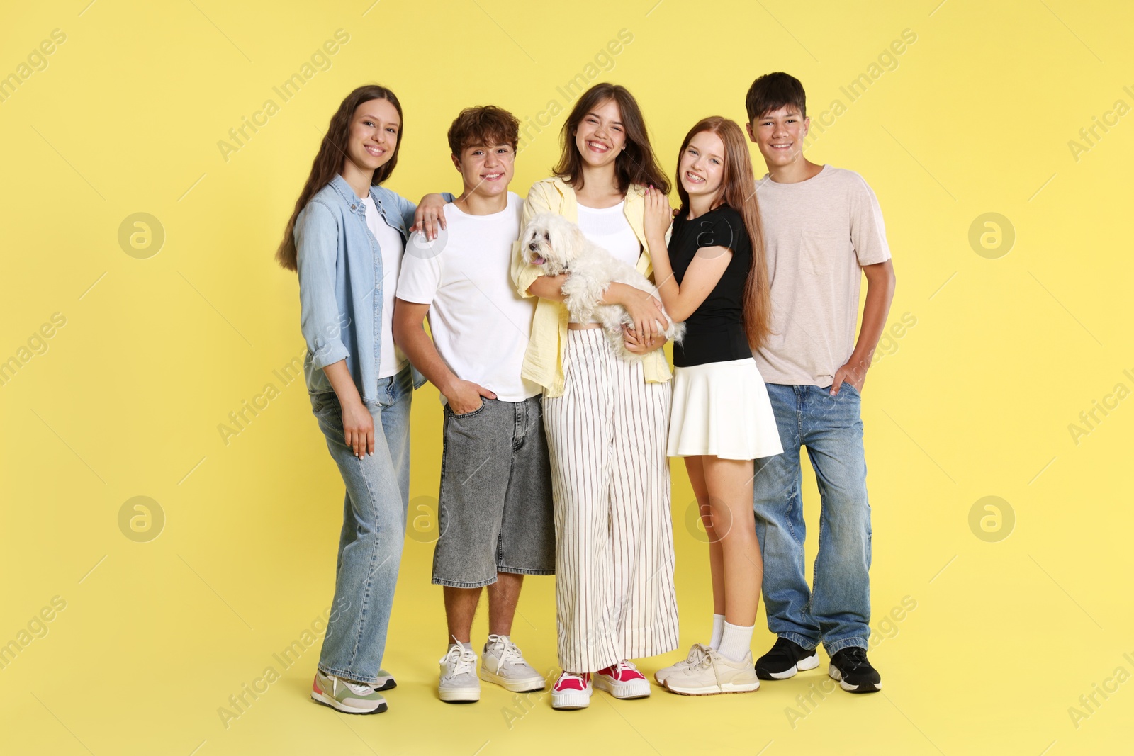 Photo of Happy teenage friends with cute dog on yellow background
