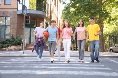 Photo of Group of happy teenage friends crossing road together outdoors