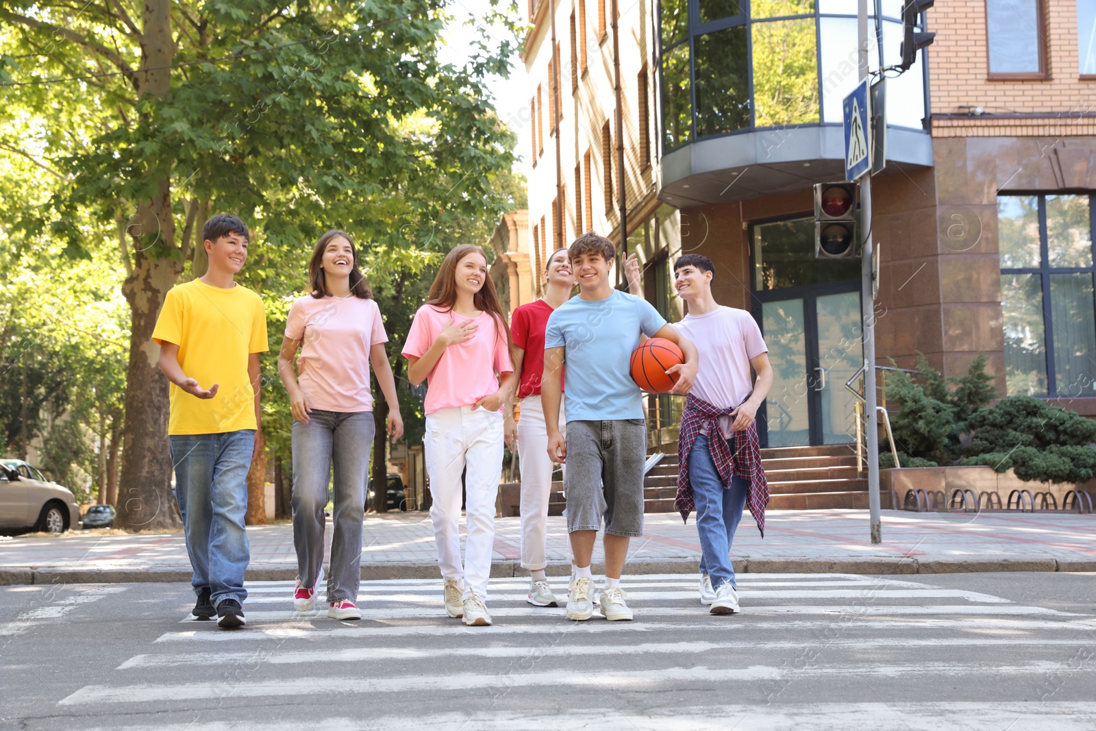 Photo of Group of happy teenage friends crossing road together outdoors