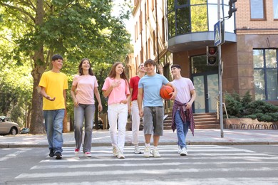 Photo of Group of happy teenage friends crossing road together outdoors